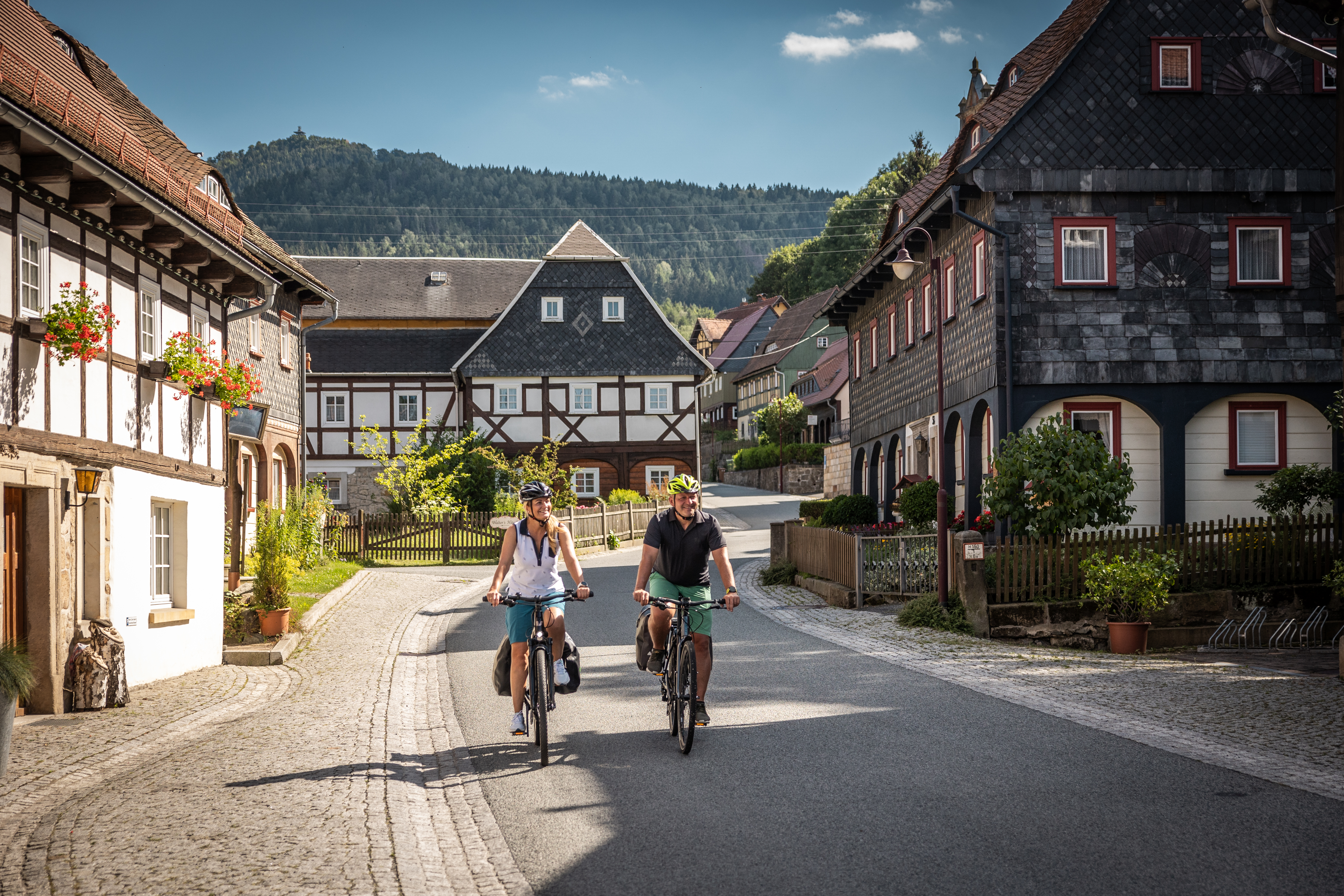 Radfahrer fahren an Umgebindehäusern vorbei